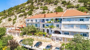 Ein mehrstöckiges Hotel mit Balkonen, einer Steinmauer und einer Hanglage im Hintergrund.