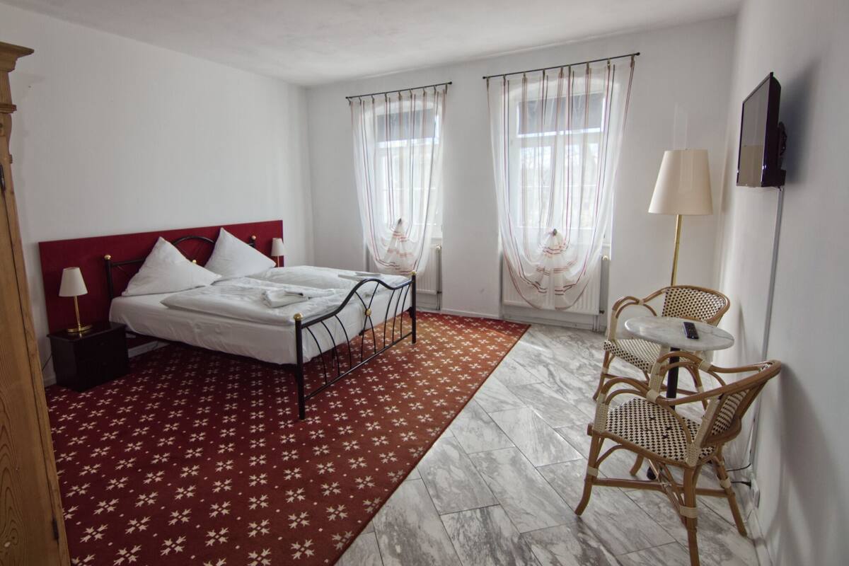 Habitación de hotel con cama, una mesita con una silla, una lámpara y un televisor en la pared.