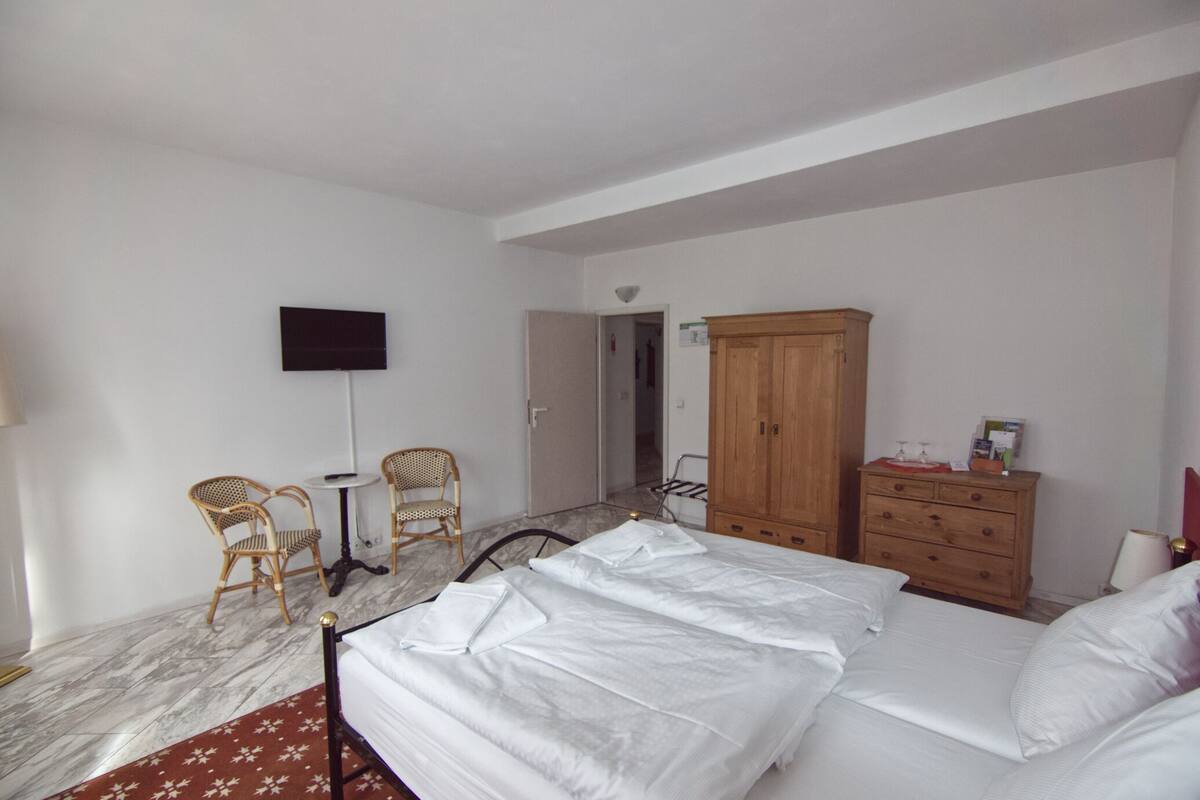 Un dormitorio con cama, dos sillas, un armario de madera, una mesita pequeña y un televisor de pantalla plana montado en la pared.