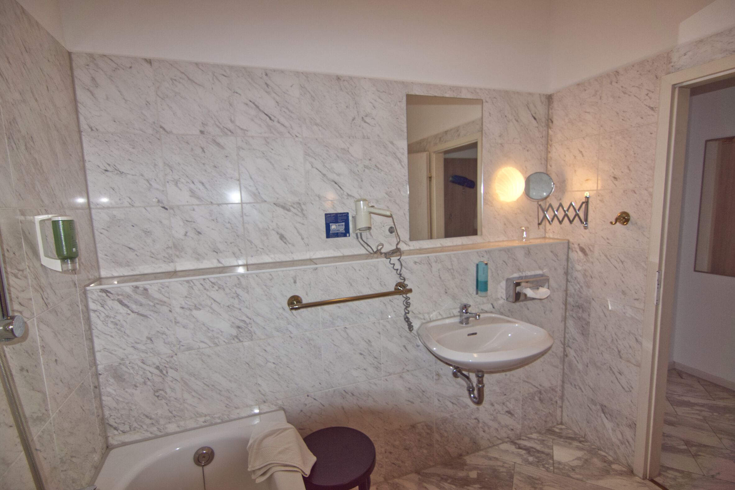 A bathroom with a marble wall, a sink, a mirror, and a towel rack.
