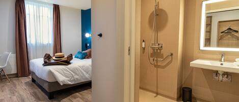 Une chambre d’hôtel comprenant un lit, une table de chevet, un miroir, une douche et un lavabo.