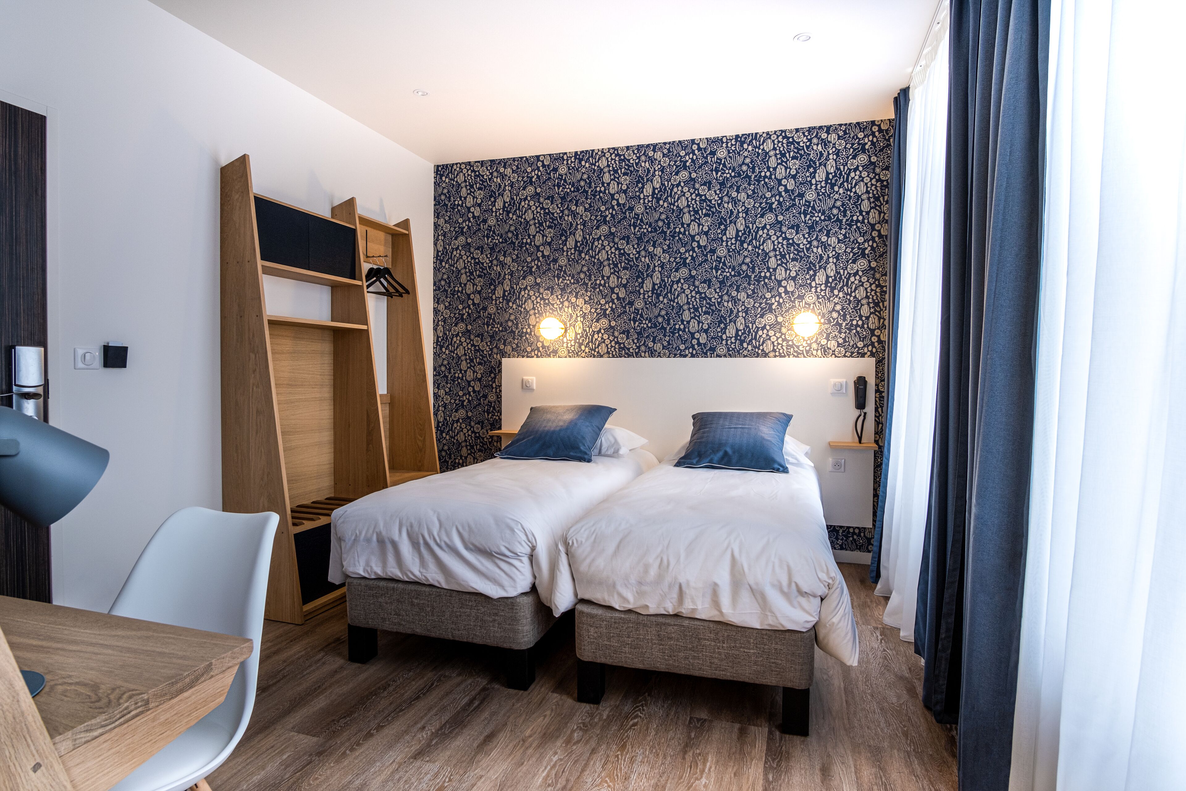 Una camera d'albergo con due letti, una scrivania, una sedia, un armadio e una parete decorata.