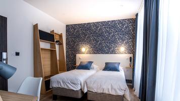 A hotel room with two beds, a desk, a chair, a wardrobe, and a patterned wall.