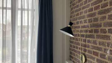 Une pièce avec un mur en briques, une fenêtre ornée de rideaux légers et une lampe fixée au mur.