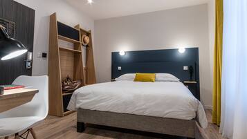 Een moderne hotelkamer met een bed, een bureau met stoel, een kledingkast en een nachtkastje met lamp.