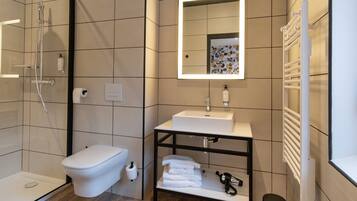 A modern bathroom with a glass-enclosed shower, a white toilet, a sink with a mirror above it, and a towel rack.