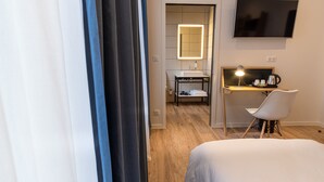 Habitación de hotel con cama, escritorio con silla, televisor en la pared y baño con espejo y lavamanos.