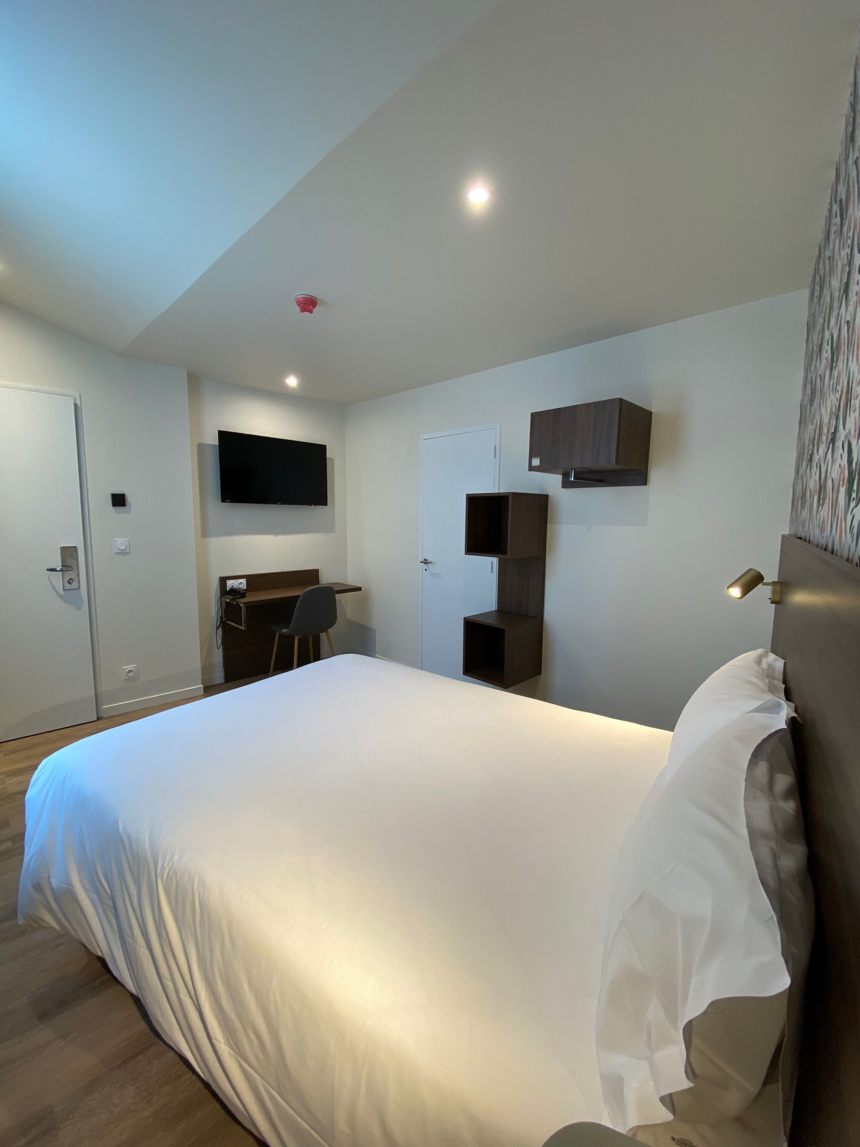 Une chambre d’hôtel moderne, dotée d’un grand lit, d’un bureau et d’un téléviseur à écran plat fixé au mur.