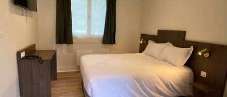 A bedroom with a bed, a bedside table, a TV mounted on the wall, and a window with curtains.