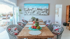 A dining area with a wooden table, patterned cushions, and a wall art collage. - Villa Bloom 2 Bedroom (Seminyak)