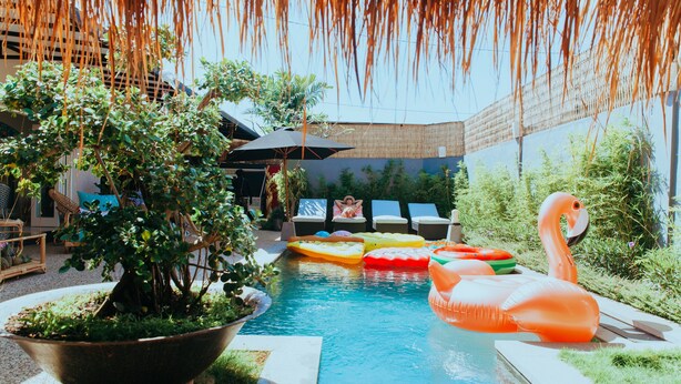 A pool area with inflatable flamingos, a large planter with greenery, and outdoor seating. - Villa Bloom 2 Bedroom (Seminyak)