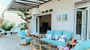 A covered outdoor seating area with wicker furniture, a glass coffee table, and a teal sofa. - Villa Bloom 2 Bedroom (Seminyak)
