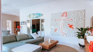 A modern living room with a light blue sofa, a wooden coffee table, and a large abstract painting. - Villa Bloom 2 Bedroom (Seminyak)