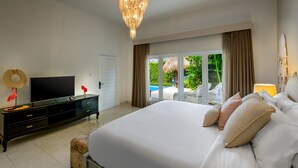 A bedroom with a large bed, a TV on a black dresser, and a view of a pool and greenery through a sliding glass door. - Villa Bloom 2,5 Bedroom (Seminyak)