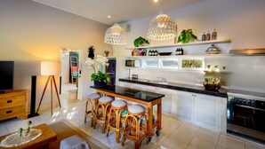 A modern kitchen with a central island, bar stools, pendant lighting, and a microwave. - Villa Bloom 2,5 Bedroom (Seminyak)