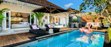 A swimming pool with a flamingo float, surrounded by outdoor seating and a covered patio area.