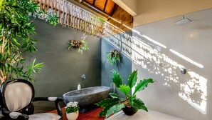 A modern bathroom with a large bathtub, a wooden chair, and several potted plants. - Villa Bloom 2,5 Bedroom (Seminyak)