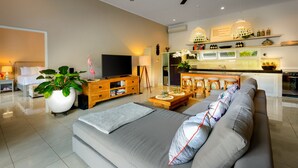 A modern living room with a sofa, TV, and a dining area with stools. - Villa Bloom 2,5 Bedroom (Seminyak)