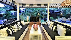 A modern living room with a large TV, black and white sofas, and a central coffee table. - Villa Bloom 4 Bedroom (Seminyak)