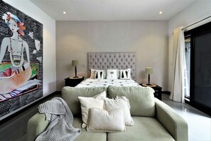 Une chambre moderne avec un grand lit, deux tables de chevet, un canapé et une grande fenêtre.