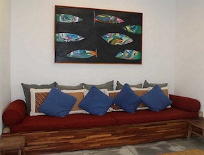 Um sofá vermelho com almofadas azuis e um quadro de um peixe emoldurado acima.