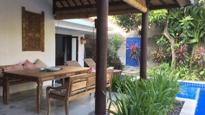 A covered outdoor dining area with a wooden table and chairs, a tiled floor, and a pool with a blue border. - Villa Mason 9 Bedroom (Seminyak)