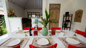 A dining area with a white table set for four, red chairs, and a decorative plant centerpiece. - Villa Mason 9 Bedroom (Seminyak)