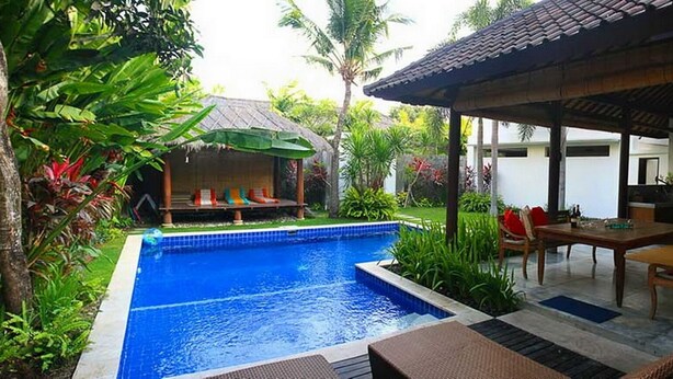Uma piscina com área de estar coberta, rodeada por vegetação exuberante e um espaço de refeições com mobiliário de exterior.