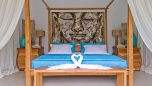 Cama com estrutura de madeira, roupa de cama azul e enfeite de cisne branco. Há duas mesas de cabeceira com luminárias e objetos decorativos.