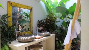 Um banheiro com duas pias de pedra, um espelho com moldura amarela e várias plantas.