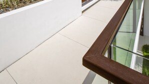 A modern outdoor area with a glass balustrade, white walls, wooden slatted screens, and a bench. - Villa Aqua (Seminyak)