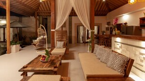 A cozy outdoor seating area with wooden furniture, a cushioned sofa, and a wicker chair. - Villa Kubu Joglo (Seminyak)