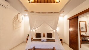 A bed with a canopy, a wooden bench, a bedside table with a plant, and a wooden door. - Villa Kubu Joglo (Seminyak)