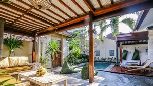 Uma área externa coberta com piscina, espreguiçadeiras e uma mesa de madeira com arranjo de flores.