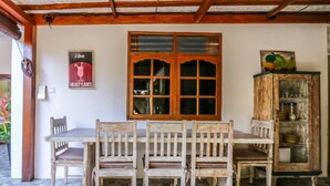 Uma área de refeições com uma mesa e cadeiras de madeira, uma janela grande com painéis de vidro e um armário com portas de vidro.