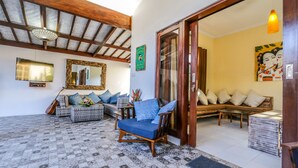 Uma sala de estar ampla com teto alto, um sofá, uma poltrona e um espelho decorativo.