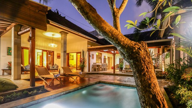 Uma área à beira da piscina com espreguiçadeiras, um espaço de refeições e um interior bem iluminado.