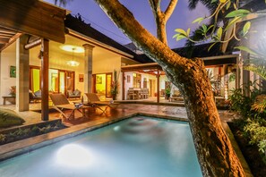 A poolside area with lounge chairs, a dining area, and a well-lit interior. - Villa Mira (Seminyak)
