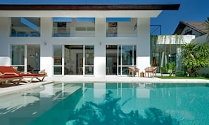 Una casa moderna con piscina, puertas de vidrio amplias y mobiliario exterior.