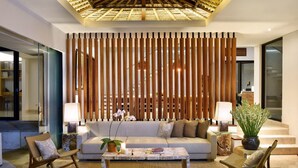 A modern living room with a sofa, coffee table, and chairs, a wooden slat partition, and a ceiling with a skylight. - Villa Serenita 3 Bedroom (Pecatu)