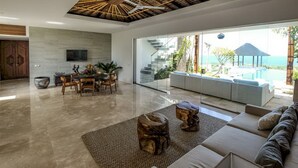 A spacious living area with a modern design, featuring a large sofa, a dining table with chairs, and a wooden coffee table. - Villa Serenita 3 Bedroom (Pecatu)