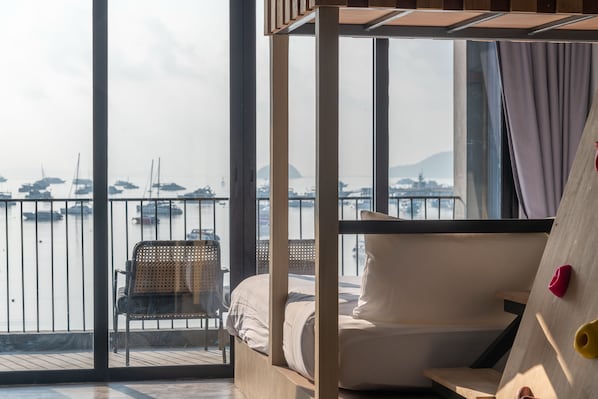A balcony with a bed, a chair, and a view of boats and water.