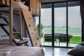 A room with a bunk bed, a climbing wall, and a view of the sea through large glass doors.