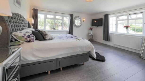 Een slaapkamer met een groot bed, een nachtkastje, een spiegel, een televisie en een raam met uitzicht op groen.
