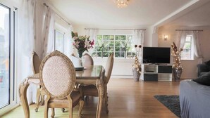 Een ruime woonkamer met een eethoek, grote ramen, een flatscreen televisie en een gezellige bank.