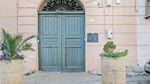 A double door with a metal grille, a beige wall, and two cylindrical planters with plants.
