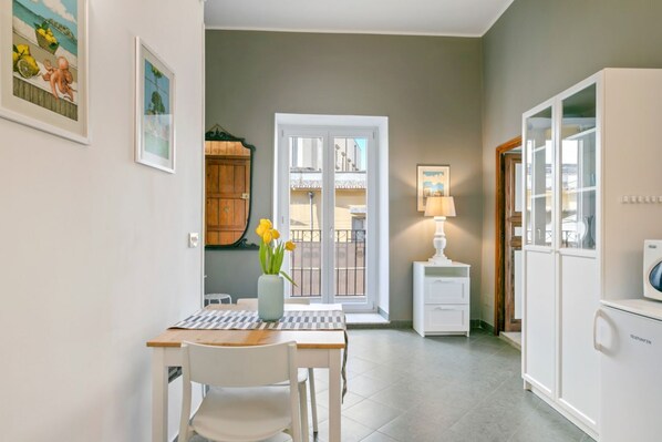 Une pièce comprenant une table à manger, des chaises, un vase avec des fleurs, une lampe, une armoire et une porte donnant sur un balcon.