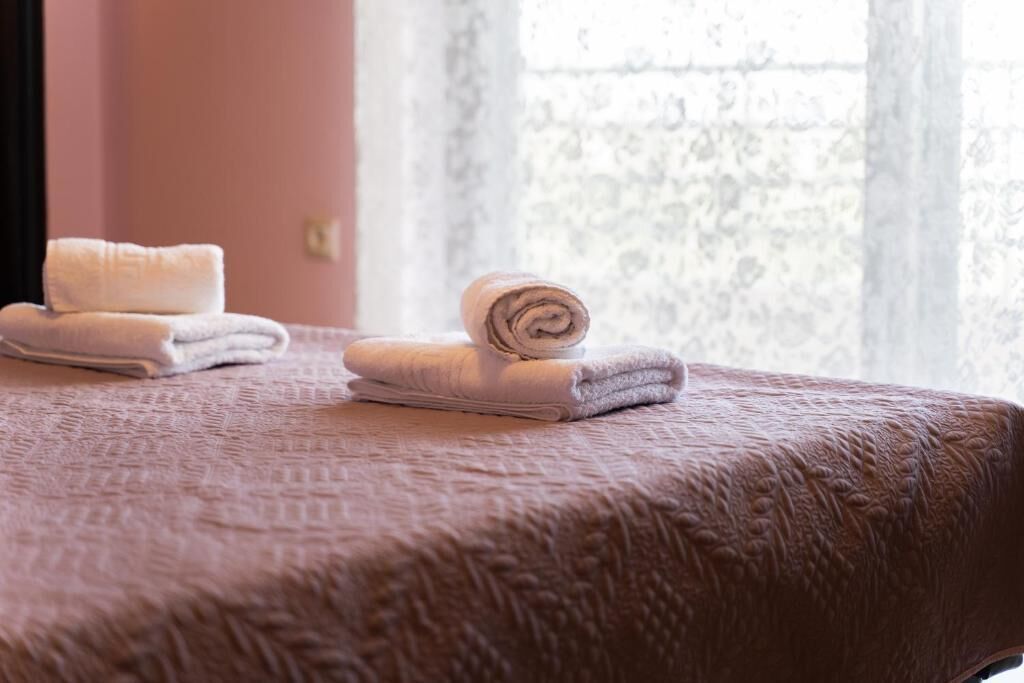 Un lit bien fait, recouvert d’une couverture rose à motifs et agrémenté de plusieurs serviettes blanches pliées.