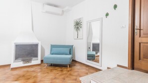 Ein Zimmer mit einem blauen Sofa, einer weißen Wand mit Spiegel, einer Holztür und einer kleinen Pflanze.