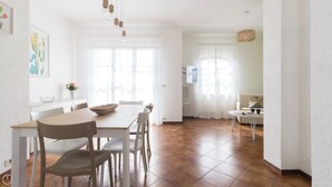 Ein geräumiger Essbereich mit Holztisch und Stühlen, einer weißen Wand mit einem gerahmten Bild und einem Fenster mit durchsichtigen Vorhängen.